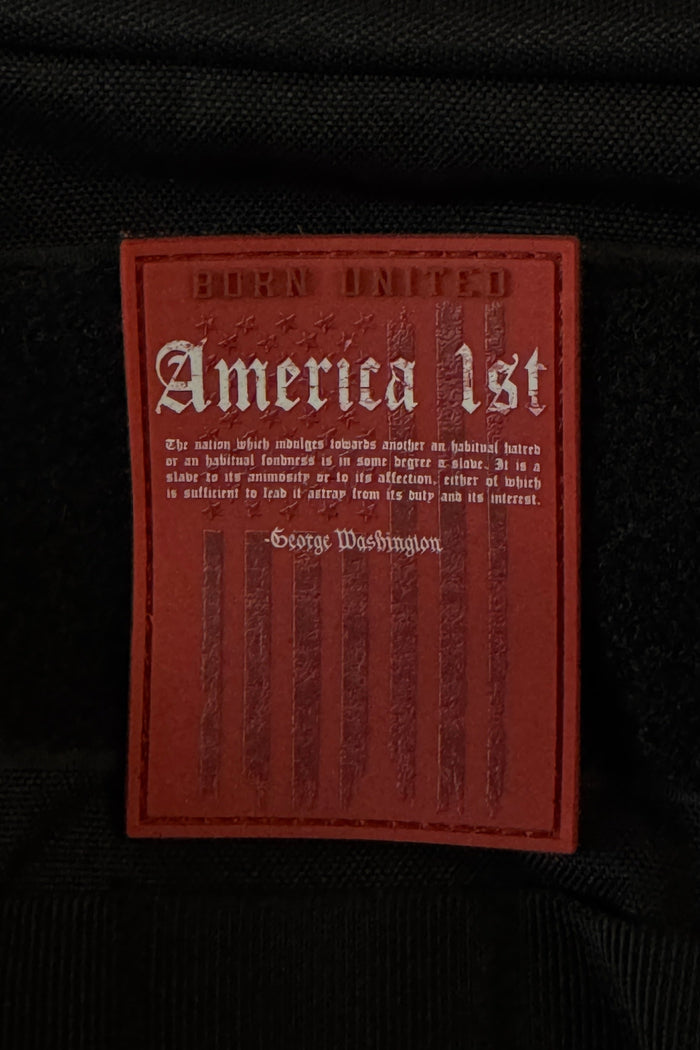 A striking black PVC patch by Born United Private Label, measuring 3 inches and equipped with Velcro, displays a bold red label featuring the text โAmerica First,โ a George Washington quote, a faded American flag motif, and โBorn Unitedโ at the top.