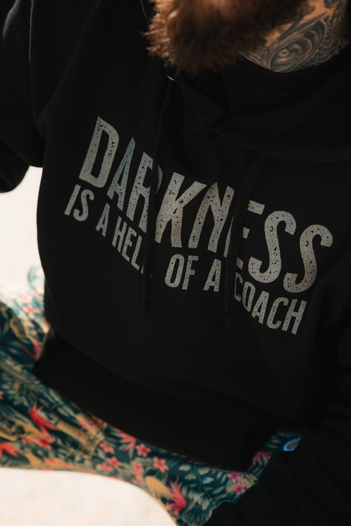 A person wears the Tango Charlie Apparel "Darkness is a Hell of a Coach" Hoodie with vibrant floral pants—stylish gym gear to inspire victory over darkness.