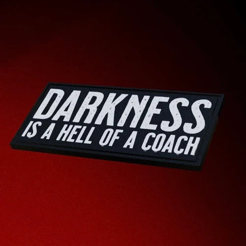 The Darkness is a Hell of a Coach Patch by Tango Charlie Apparel features bold white text on a rectangular PVC design with Velcro backing for easy attachment.