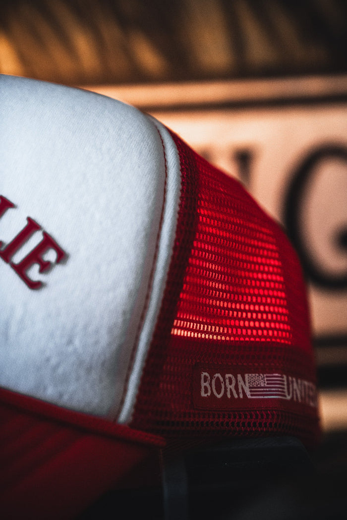 Close-up of the I Am Charlie Red Trucker Snapback by Born United Private Label. This 5-panel snapback features red and white mesh panels, a curved brim, and "Born United" embroidery beside a small American flag.