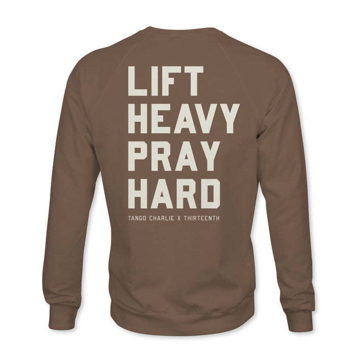 The Lift Heavy. Pray Hard. - Crewneck from Tango Charlie Apparel features bold white text on the back with "Lift Heavy Pray Hard" and smaller TANGO CHARLIE X THIRTEENTH below, displayed on a brown sweatshirt against a clean white background.