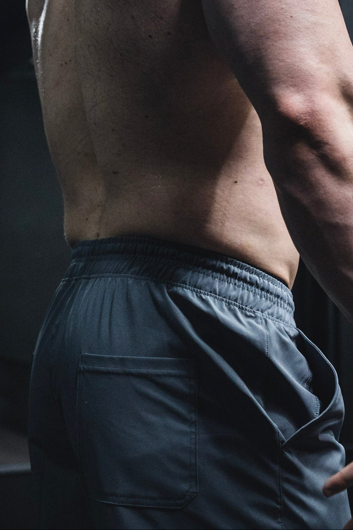 A close-up of a shirtless person from the waist up, wearing Born United Private Label Men's Standard Performance Shorts | 5.5" in Gunmetal Gray, featuring an elastic waistband and back pocket.