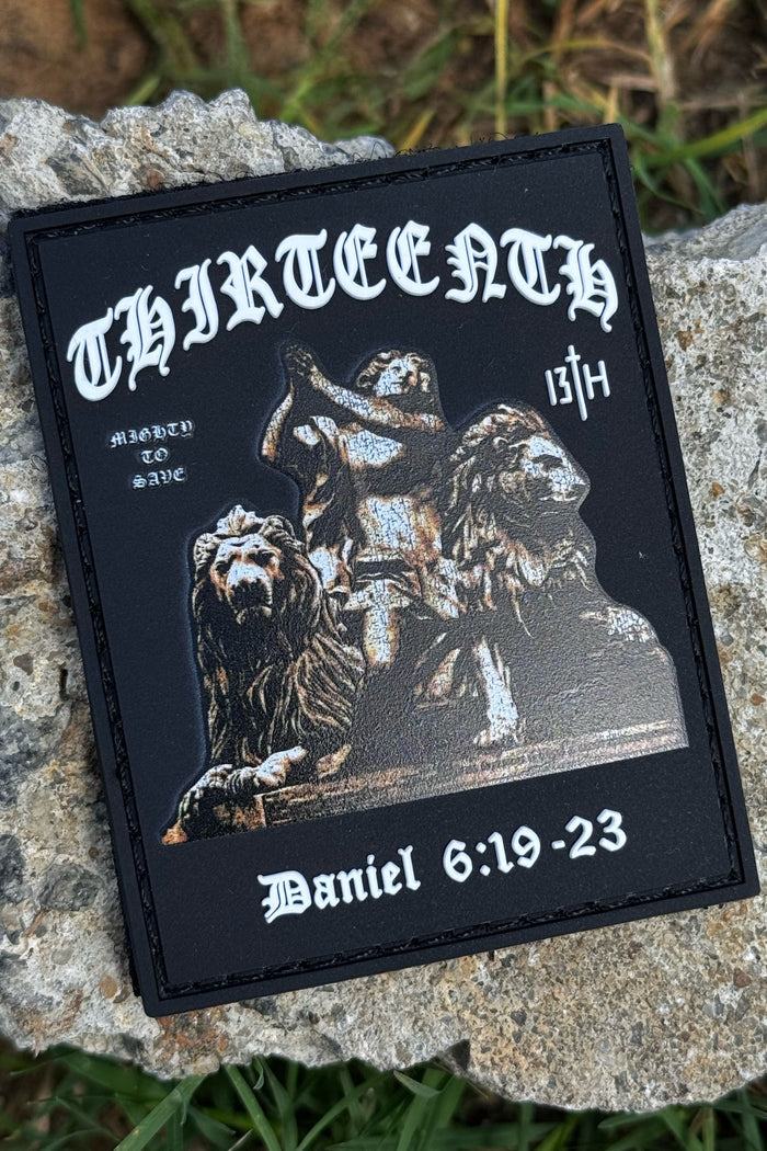 The 13th Mighty to Save PVC Patch shows Daniel in the lions’ den, with THIRTEENTH at the top, Marked to Save and 13th on the sides, Daniel 6:19-23 at the bottom, and rests on a rock.