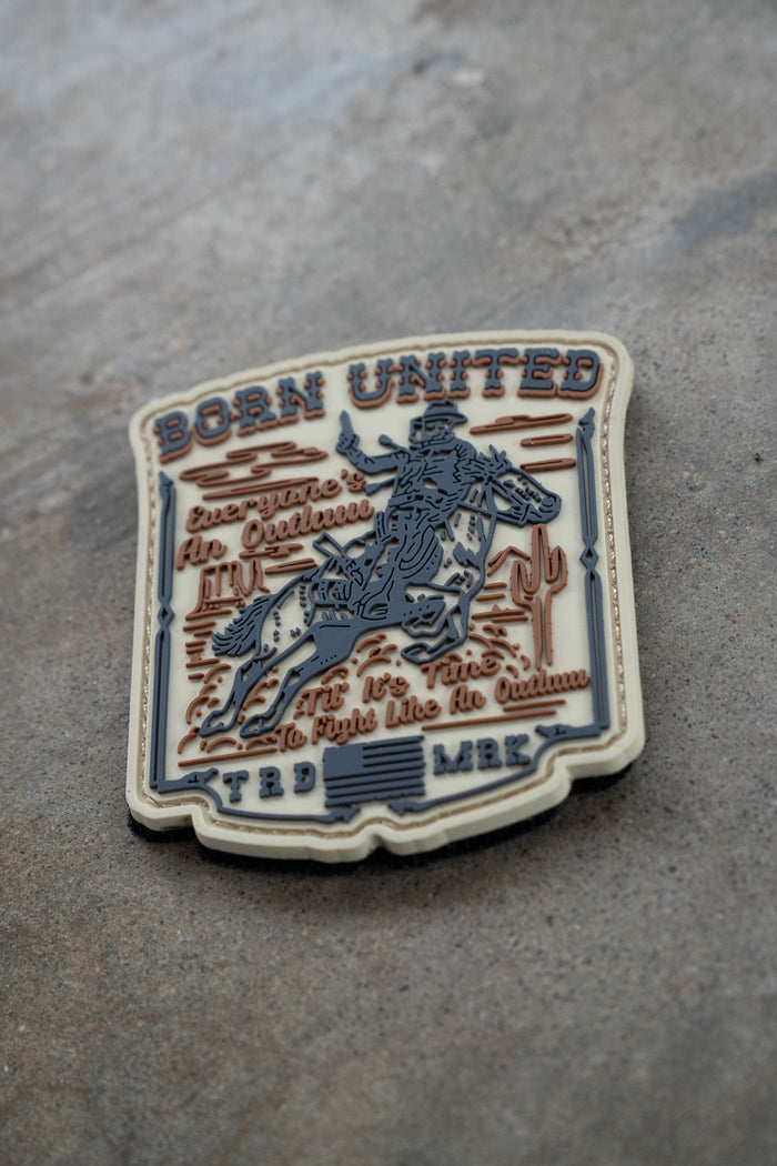 The Outlaw PVC Patch by Born United Private Label features a cowboy riding a bucking horse with cacti and stars, plus the phrases "Born United," "Everyone in Oklahoma," and "To fight like an Okie" on a stone background.