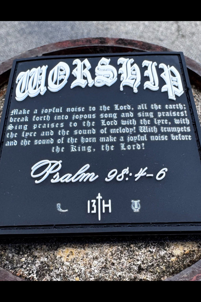 The Worship PVC Patch by 13th features Psalm 98:4-6 in ornate white text on black, with 13TH and two small symbols at the bottom, shown resting on a stone surface.