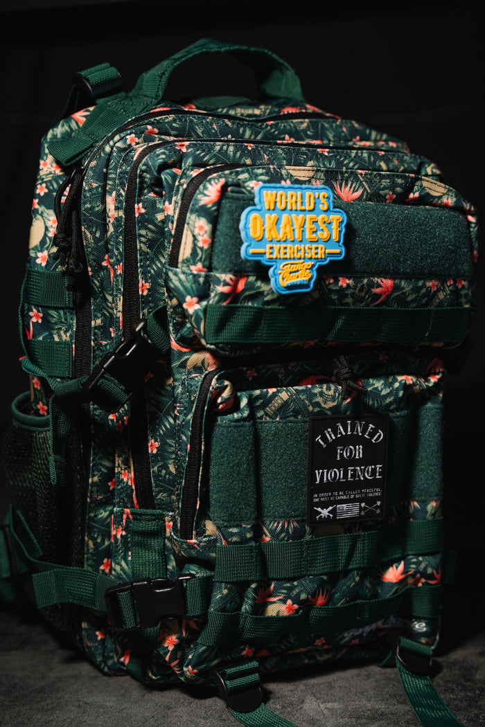 Aloha AR - Tac Pac 25L by Tango Charlie Apparel: a dark green floral-patterned hunting backpack with two patches—WORLDS OKAYEST EXERCISER and TRAINED FOR VIOLENCE—plus multiple zippers and straps.