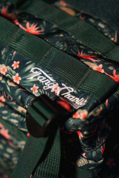 Close-up of the Tango Charlie Apparel Aloha AR - Tac Pac 25L, a dark green waterproof backpack with a floral pattern, featuring textured material, a strap, black plastic buckle, and sewn white logo.