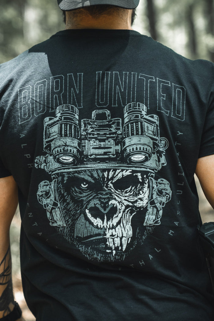 A man outdoors, seen from behind, wears the Alpha Mentality shirt by Born United Private Label—a bold black tee with a fierce gorilla in night-vision goggles and “BORN UNITED” above, embodying confidence and strength.
