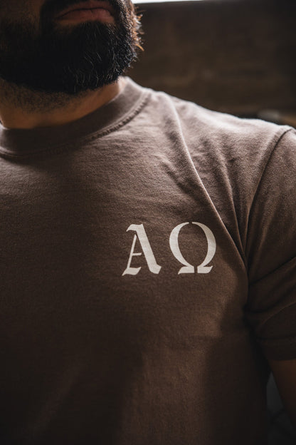 A bearded person wears the 13th Alpha & Omega Premium Oversized Tee in Espresso, showcasing white ΑΩ symbols on the chest. The image highlights the shirt's unique design by focusing on the upper torso.