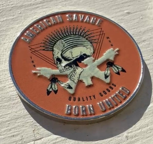 A round, textured American Savage Challenge Coin by Born United Private Label showcases a skull with a mohawk and feathered crossed bones. It features the text American Savage, True Next, Quality Goods, Born United.
