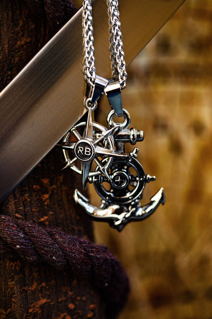The Relentless Betrayals Anchors Aweigh Necklace features meticulously handcrafted silver pendants with a compass rose and anchor design. They hang from a durable stainless steel chain on a textured brown background, offering elegance and peace of mind with a lifetime warranty.