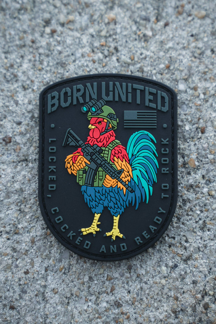 The Battle Bird PVC Patch by Born United Private Label features a colorful rooster in military gear with a rifle, “BORN UNITED” at the top, and “LOCKED, COCKED AND READY TO ROCK” at the bottom, set against a rough concrete surface.