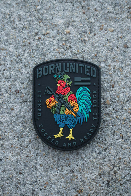 The Battle Bird PVC Patch by Born United Private Label shows a vibrant rooster in a helmet with a rifle. It reads "BORN UNITED" on top and "LOCKED, COCKED AND READY TO ROCK" below, all set against a rough concrete backdrop.