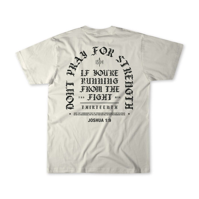 Introducing the Be Strong Premium Tee by 13th—a white, high-quality shirt featuring bold black gothic-style text on the back: “Don’t pray for strength if you’re running from the fight,” referencing Joshua 1:9. This powerful statement piece is a standout addition to our faith apparel collection.