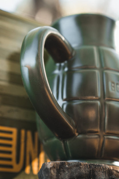 The BU Sip Sip Boom Mug by Born United Private Label features a dark green, hand grenade-shaped design with a handle like a safety lever—set against a blurred gold and green background, it’s an unforgettable conversation starter.