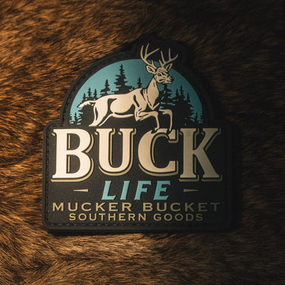 A Buck Life PVC Patch by Mucker Bucket featuring an image of a buck and trees rests on a brown fur surface.