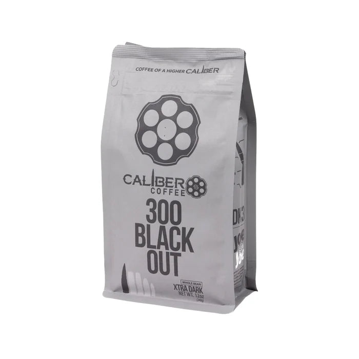 A silver coffee bag labeled Caliber Dark Roast 300 Blackout - Whole Bean by Caliber Coffee Company, features a revolver cylinder logo and bullet illustrations. Text reads Coffee of a Higher Caliber and Extra Dark Roast Net Wt. 12oz, highlighting its specialty-grade, single-origin excellence.