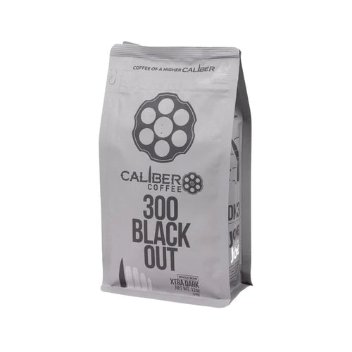 A silver coffee bag labeled Caliber Dark Roast 300 Blackout - Whole Bean by Caliber Coffee Company, features a revolver cylinder logo and bullet illustrations. Text reads Coffee of a Higher Caliber and Extra Dark Roast Net Wt. 12oz, highlighting its specialty-grade, single-origin excellence.
