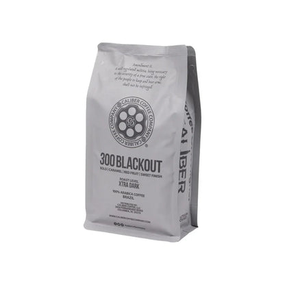 A 300 Blackout bag from Caliber Coffee Company offers a specialty-grade, single-origin dark roast with bold caramel and red fruit notes and a sweet finish. Packaged in gray with black text, its made from 100% Arabica beans from Brazil.