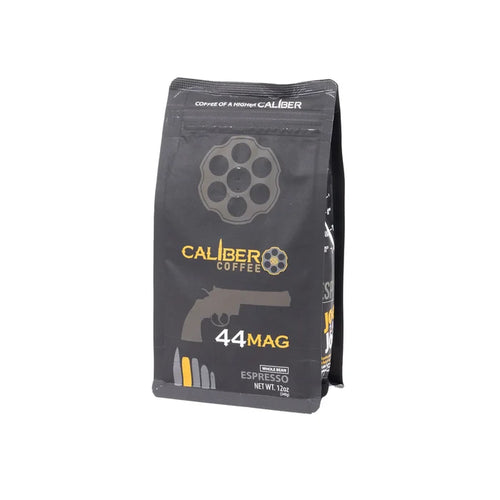 A black package of Caliber Coffee Company features gun-themed graphics, including a revolver chamber and handgun silhouette. The label on Caliber Espresso Roast .44 Mag - Whole Bean displays a net weight of 12 oz, highlighting artisan roasted, 100% Arabica beans for specialty grade coffee lovers.