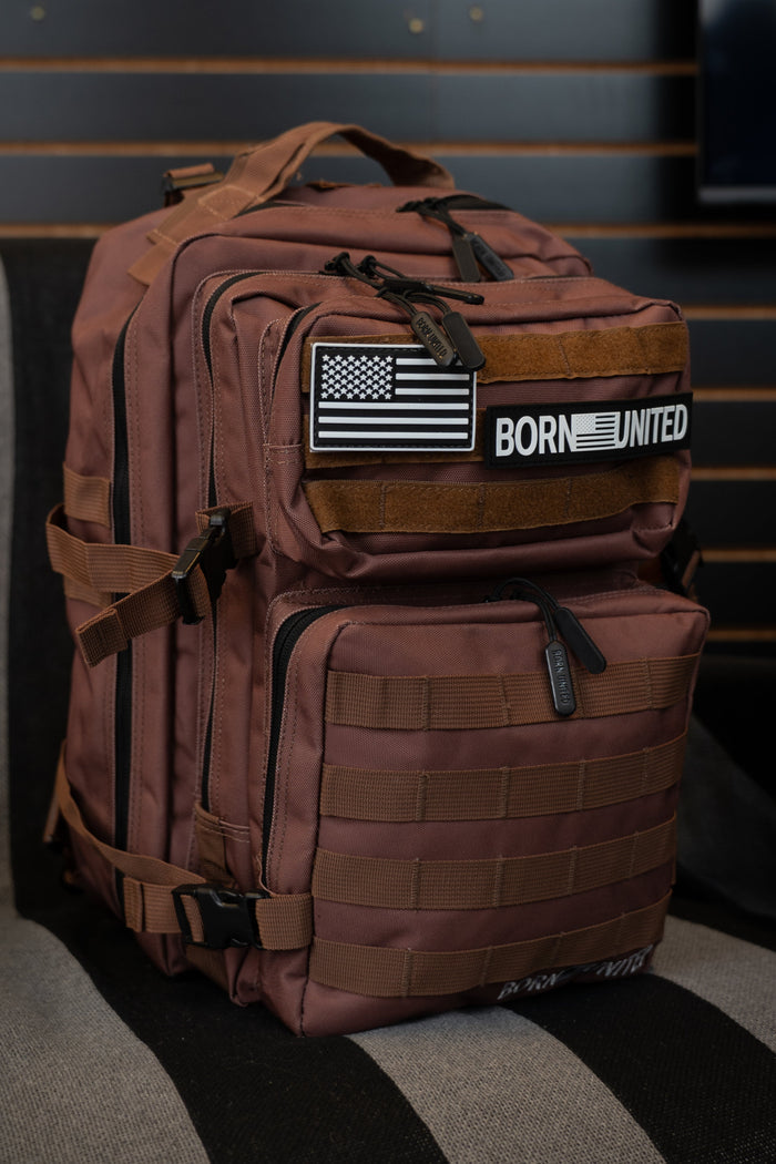 The Chocolate Tac-Pac - 25L from Born United Private Label is a brown TSA-approved tactical backpack featuring multiple compartments, MOLLE webbing, and a front patch with an American flag and the words "BORN UNITED," providing organized storage for all your gear.