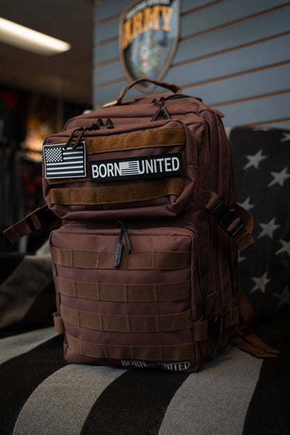 A Born United Private Label Chocolate Tac-Pac - 25L tactical backpack, featuring “BORN UNITED” and American flag patches, rests on a star-patterned chair and displays its organized storage compartments; an Army sign appears in the background.