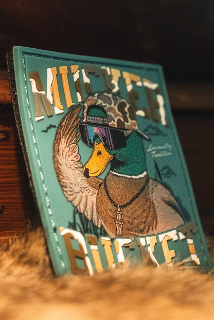 The Cool Duck PVC Patch from Mucker Bucket features a 3D design of a duck sporting a helmet, goggles, and dog tags, with MILKYET and BUCKET displayed in bold metallic lettering.