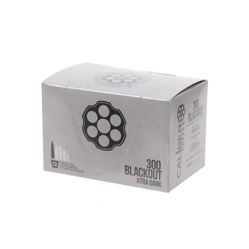 A silver box labeled Dark Roast 300 Blackout Single-Serve Shells by Caliber Coffee Company, featuring bullet and revolver cylinder illustrations. Contains 12 servings of specialty dark roast coffee, totaling 4.9 ounces (139.2 grams).