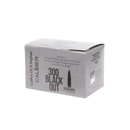 A gray rectangular box of specialty grade coffee from Caliber Coffee Company is labeled Dark Roast 300 Blackout Single-Serve Shells. The design mimics ammo packaging with Coffee of a Higher Caliber text, plus rights protection and logo details on the side.