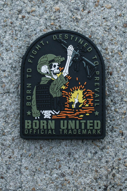 The Destined to Prevail PVC Patch by Born United Private Label features a skeleton in military gear with a rifle amid an explosion and the words “BORN TO FIGHT, DESTINED TO PREVAIL. BORN UNITED OFFICIAL TRADEMARK.” Ideal for tactical gear.