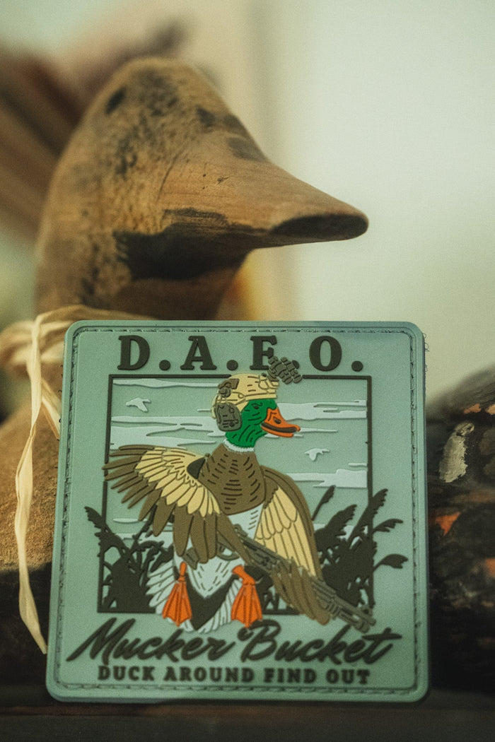 A square embroidered patch featuring a duck illustration and the text 'D.A.