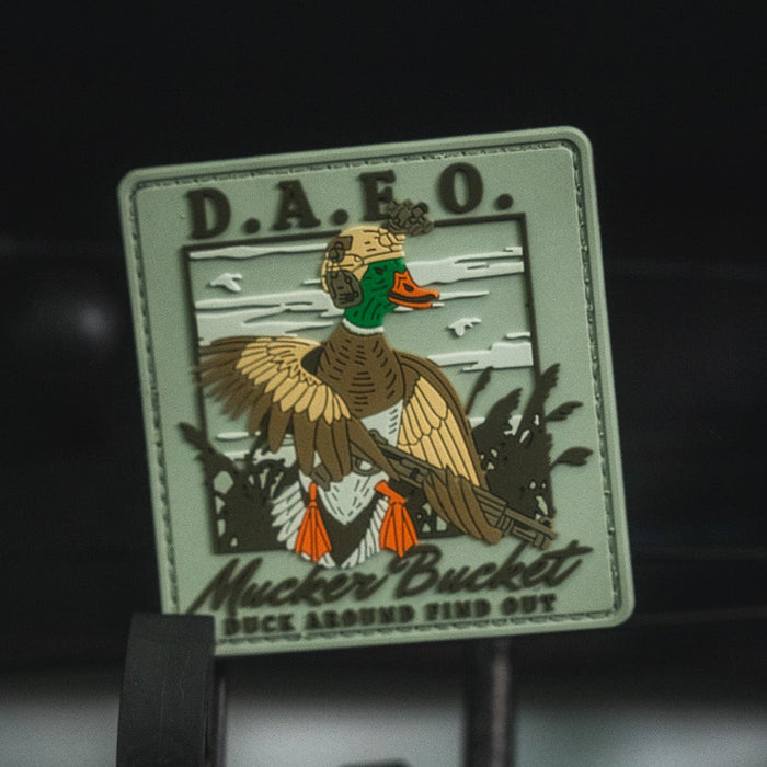 The Mucker Bucket Duck Around & Find Out PVC Patch is a rugged 4x4 inch 3D Velcro patch featuring a tactical duck with rifle on a green reed background, highlighted by the bold text D.A.F.O. and "Duck Around Find Out" for added style and durability.