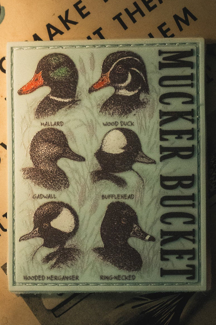 The Mucker Bucket Duck DNA PVC Patch features illustrations of six duck species—Mallard, Wood Duck, Gadwall, Bufflehead, Hooded Merganser, and Ring-necked—and is perfect for pairing with a 4x4 patch or displaying alongside your favorite Velcro patch collection.
