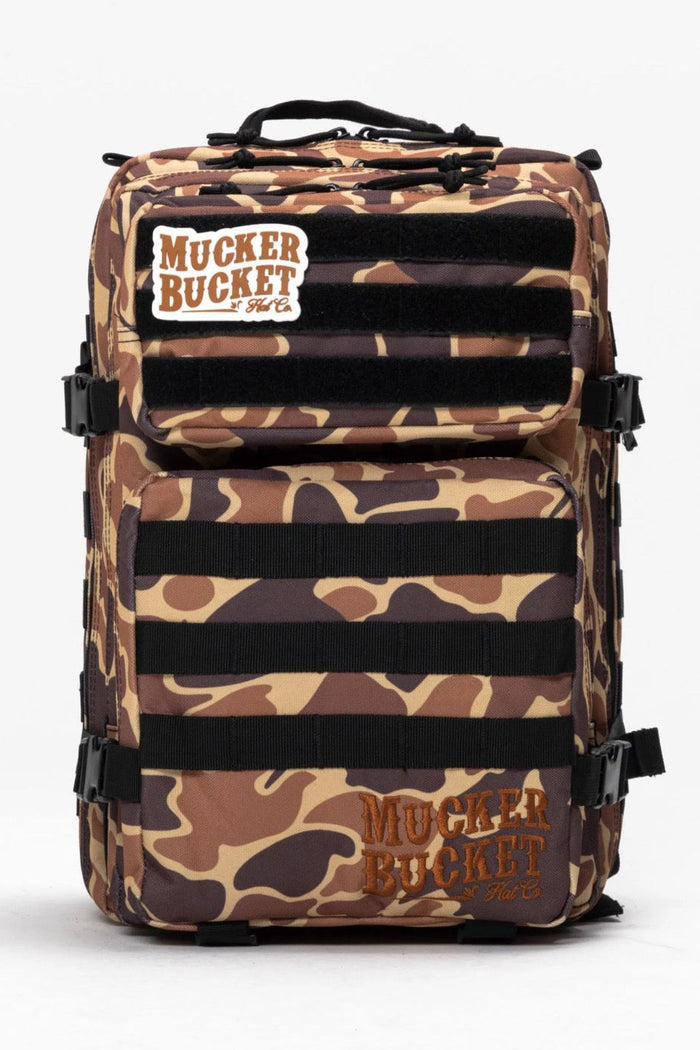 The Mucker Bucket Duck It Limited Edition Tac-Pac - 25L features a camouflage pattern, branded patches, and multiple straps and compartments—standing out against a plain white background.