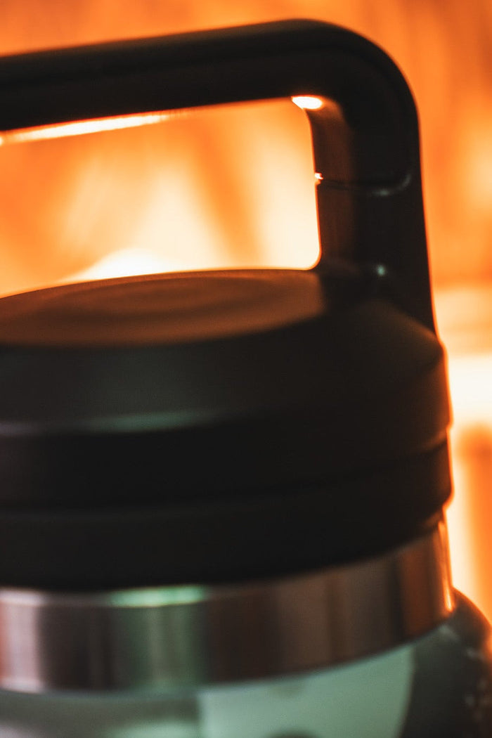 Close-up of the leak proof lid with handle on the Mucker Bucket Duck Jug—Duck Camo Water Bottle (26oz), black and silver stainless steel, set against a warm, blurred background.