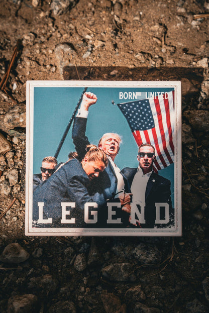 A square coaster has a stylized image of a suited man with a raised fist, surrounded by others, with an American flag visible. It features the text BORN UNITED and Forever Legend - Trump PVC Patch by Born United Private Label.