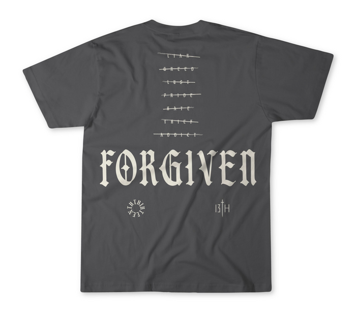 The Forgiven Premium Tee by 13th features "FORGIVEN" in bold Gothic font on the back, a barbed wire graphic above, and small symbols below—including a circular design, "13TH" initials, and subtle references to overcoming addiction or lying.