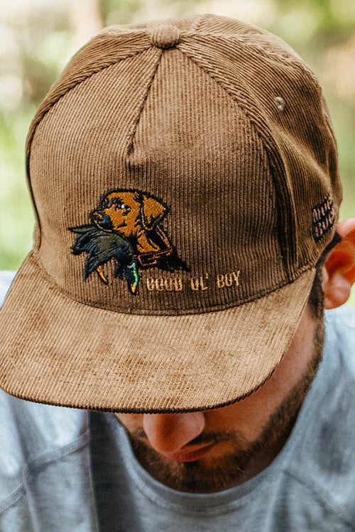 Man wearing a brown cap with a bear design and text in a forest setting