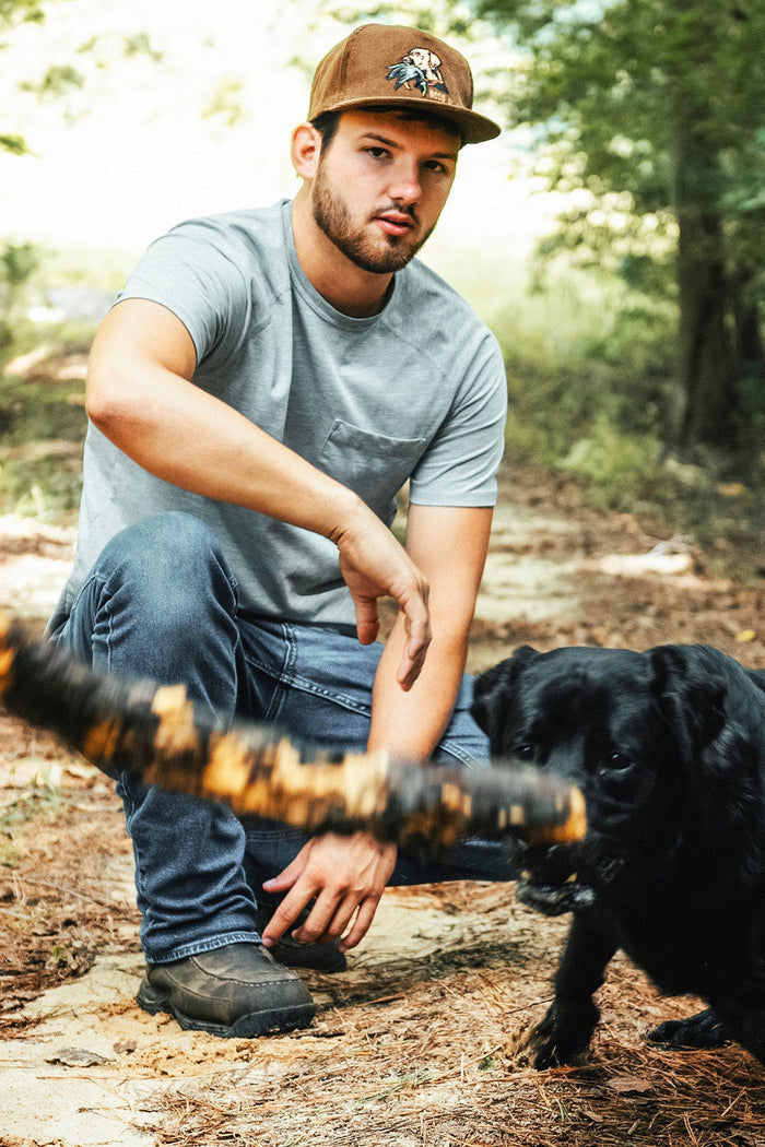 Man sitting on a forest path with a black dog holding a frisbee