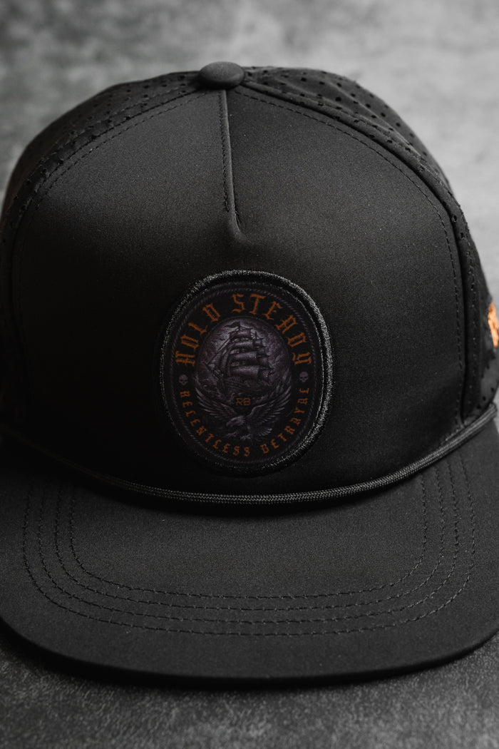 A close-up of the Hold Steady Ghost Snapback by Relentless Betrayal—a premium snapback baseball cap with a round patch reading HOLD STEADY BREATHLESS BETRAYED in orange and showcasing a coiled snake.