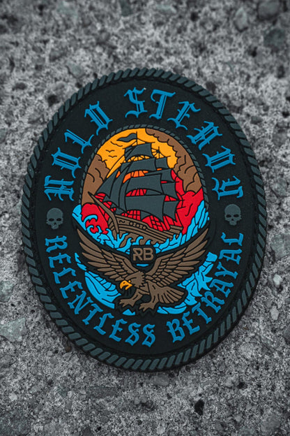The Hold Steady Patch by Relentless Betrayal is a colorful 3x3 Velcro patch showing a sunset ship above an eagle, with "HOLD STEADY" on top, "RELENTLESS BETRAYAL" below, skulls, and the initials RB on rough gray ground.