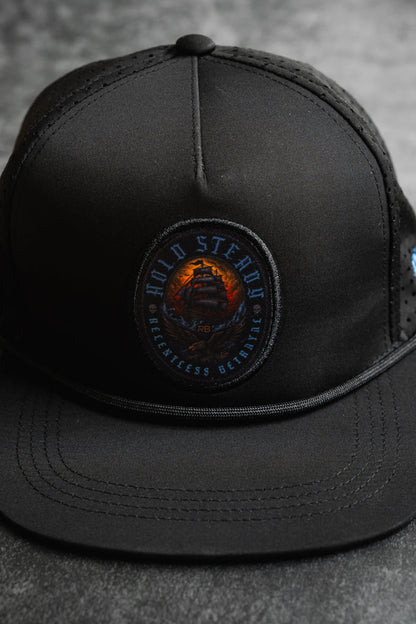 The Relentless Betrayal Hold Steady Snapback is a black baseball cap with a circular ship patch and "Hold Steady, Relentless, and Reliable" embroidered around the edge.