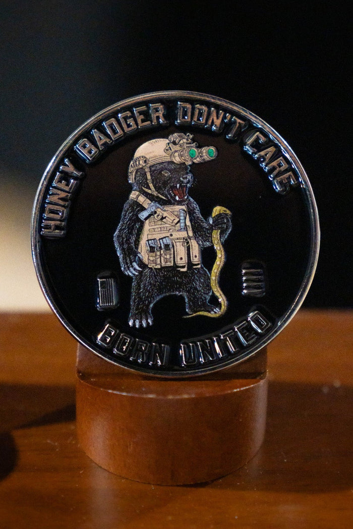 The Honey Badgerin' Challenge Coin by Born United Private Label features an armored honey badger with a snake and night-vision goggles, plus "HONEY BADGER DONT CARE" and "CUBAN UNITED" text around the edge, shown on a wooden stand.
