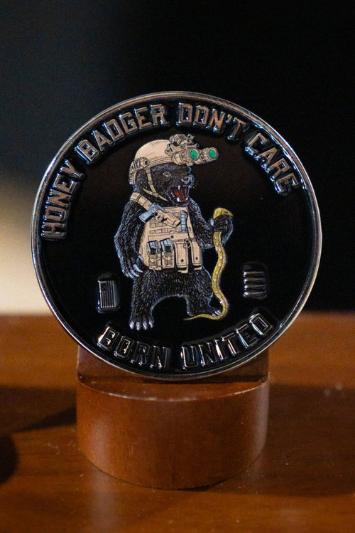 The Honey Badgerin' Challenge Coin by Born United Private Label features an armored honey badger with a snake and night-vision goggles, plus "HONEY BADGER DONT CARE" and "CUBAN UNITED" text around the edge, shown on a wooden stand.
