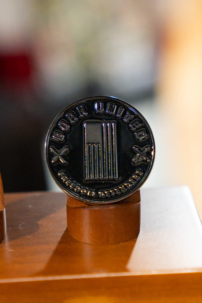 A close-up of the round, black Honey Badgerin' Challenge Coin by Born United Private Label, featuring a pillar design with "BODY UNITED" and "ACCEPT NO DEFEATS" engraved, shown on a wooden stand. Ideal for collectors and Honey Badger fans.