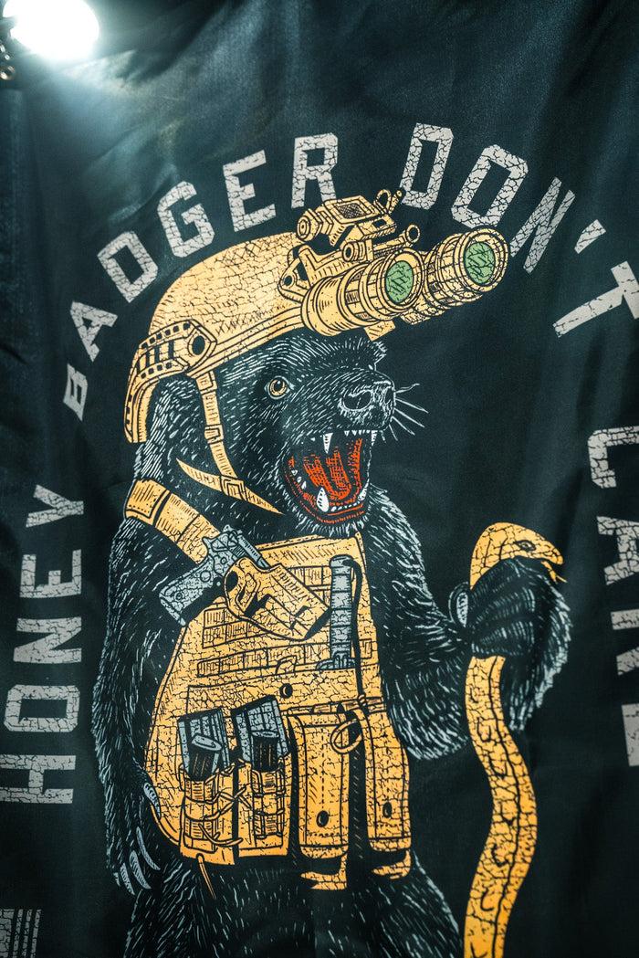 The Born United Private Label Honey Badgerin' Flag features a fearless honey badger in tactical gear and night-vision goggles holding a snake, with “HONEY BADGER DON’T CARE” around the image, printed on durable polyester.