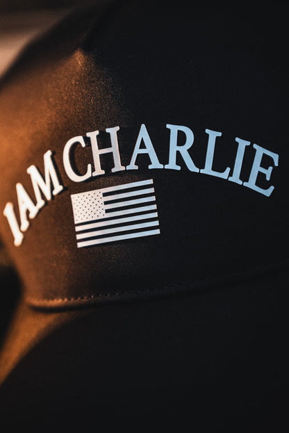 A close-up of the Born United Private Label I Am Charlie Black Snapback, a 5-panel curved bill cap with white "I AM CHARLIE" text above a stylized white American flag.