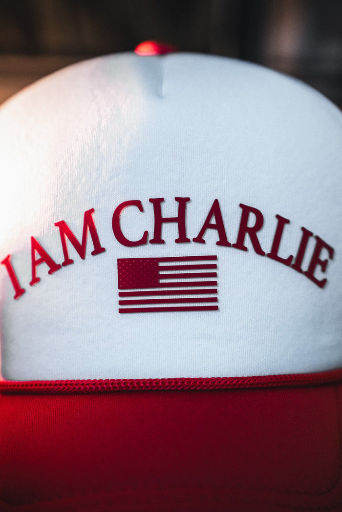 A close-up of the Born United Private Label "I Am Charlie Red Trucker Snapback," featuring "I AM CHARLIE" and an American flag in red on the white and red front.