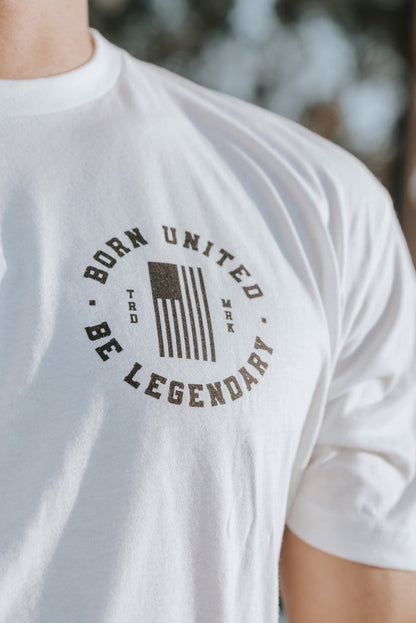 Close-up of an individual sporting the Im Back - #47 - White tee by Born United Private Label, featuring a stylized flag and Born United Be Legendary, symbolizing hope for a Trump 2024 win. Trees are blurred in the background.