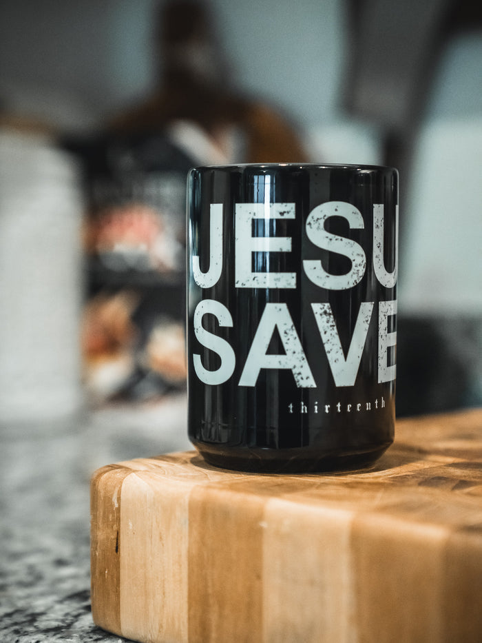 A 13th Jesus Saves Mug with bold white text is displayed on a wooden cutting board in a warm kitchen setting.